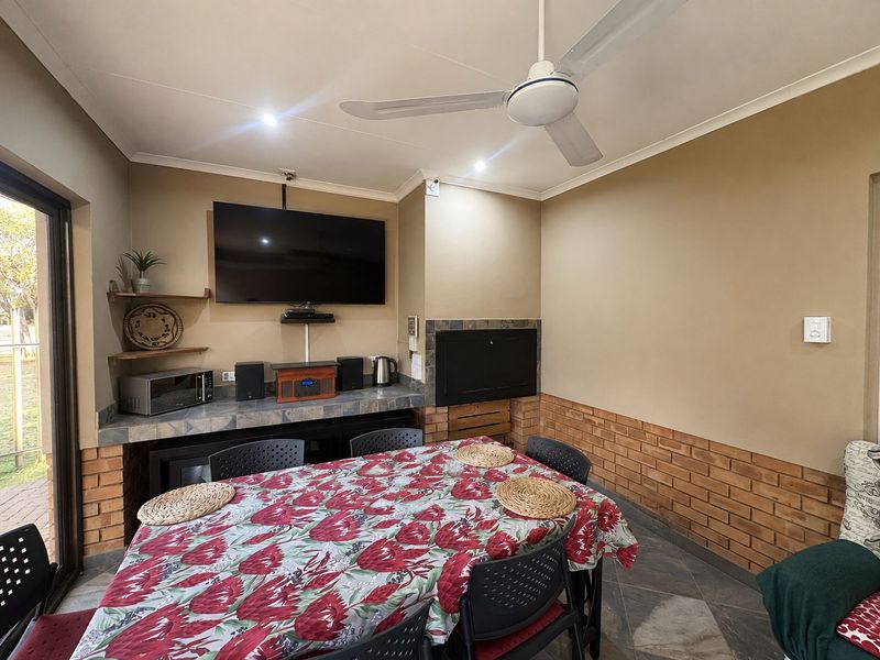 Covered patio area featuring a built-in braai, exposed brick accents, tiled flooring, and a ceiling fan, providing a functional space for outdoor dining and entertainment.