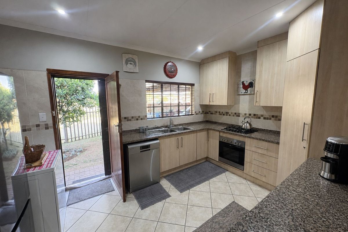 A well-maintained kitchen featuring light wood cabinetry, granite countertops, built-in oven, gas hob, and direct access to the rear garden.