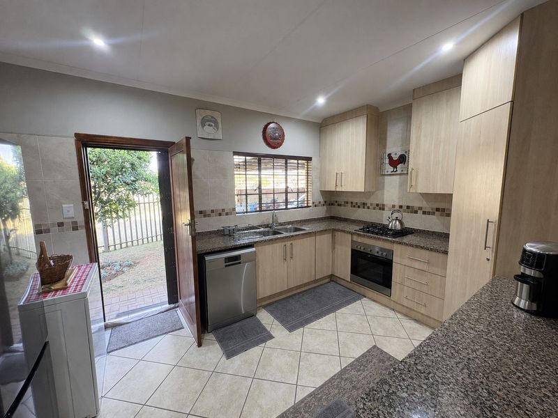 A well-maintained kitchen featuring light wood cabinetry, granite countertops, built-in oven, gas hob, and direct access to the rear garden.
