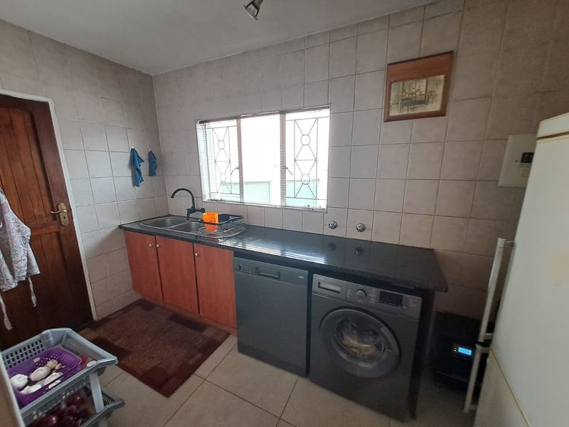 Functional laundry room featuring a double basin sink, dark granite countertops, tiled splashbacks, and dedicated space for under-counter appliances.