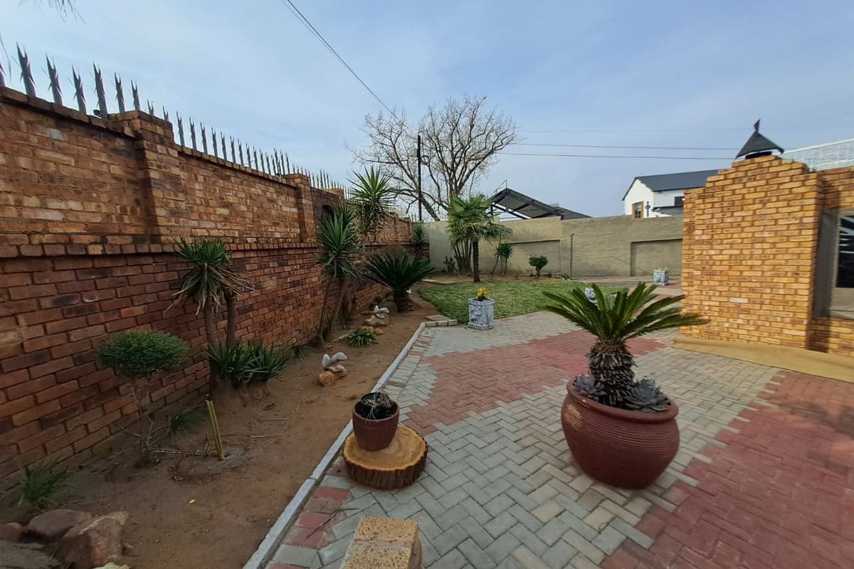 A private rear courtyard featuring a paved patio area, established garden beds, and a secure brick boundary wall with integrated security spikes.
