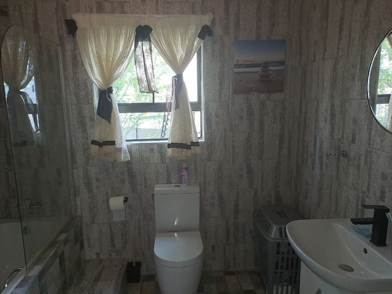 A functional bathroom featuring a shower enclosure, toilet, and vanity basin with modern tiled finishes throughout.