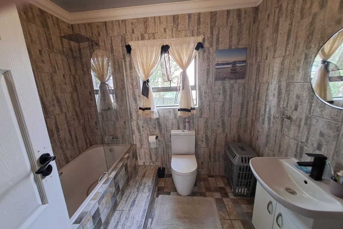 A functional bathroom featuring a bathtub with a glass screen, a wall-mounted rain shower, a toilet, and a vanity unit with a basin.