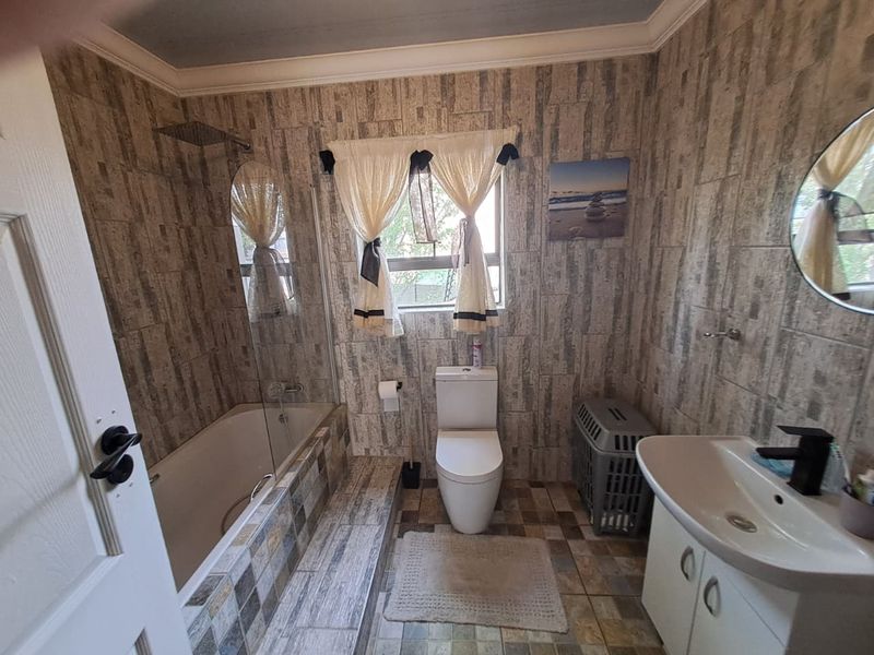 A functional bathroom featuring a bathtub with a glass screen, a wall-mounted rain shower, a toilet, and a vanity unit with a basin.