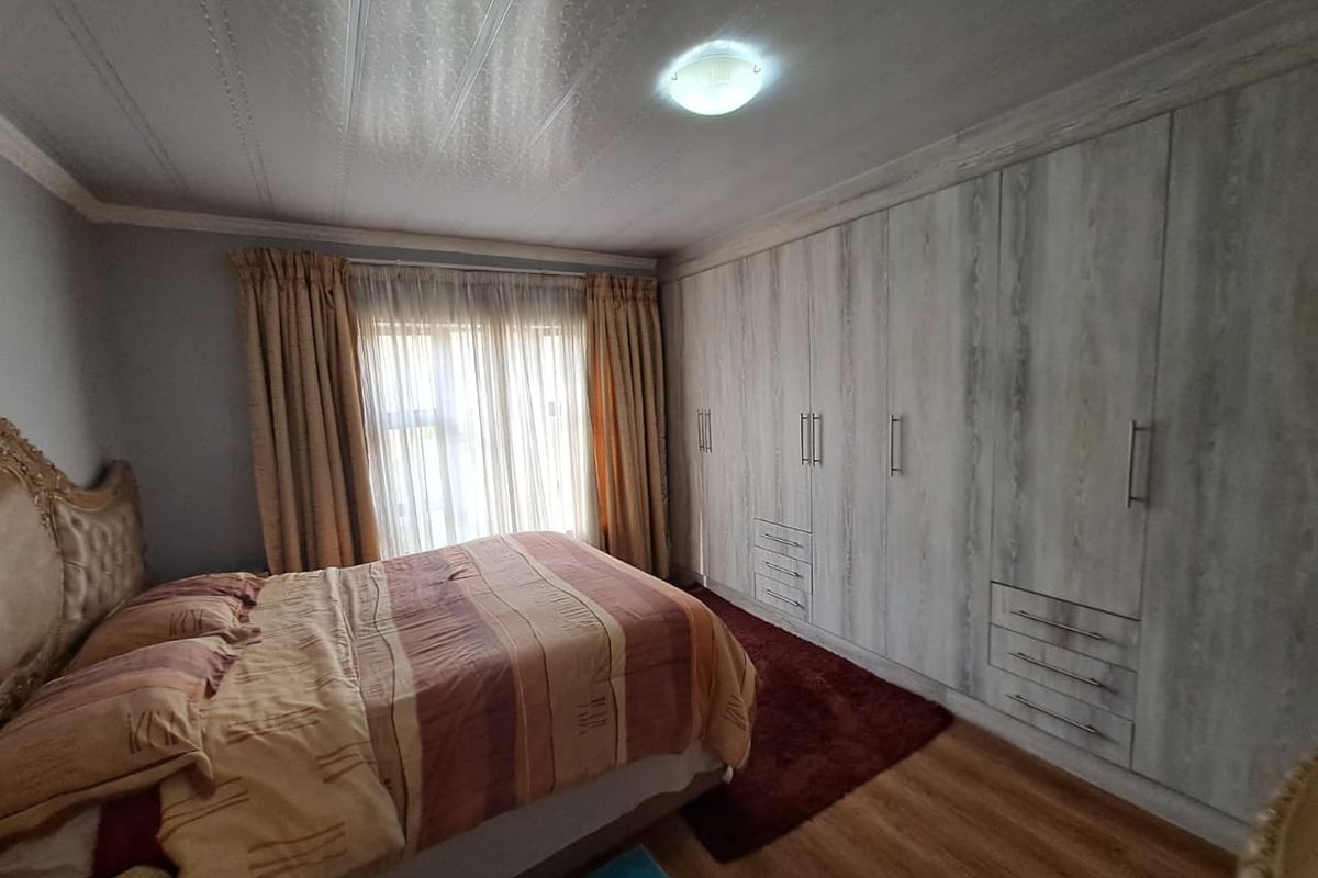 A well-maintained bedroom featuring extensive built-in cupboards with a light wood finish, laminate flooring, and a neutral color palette.