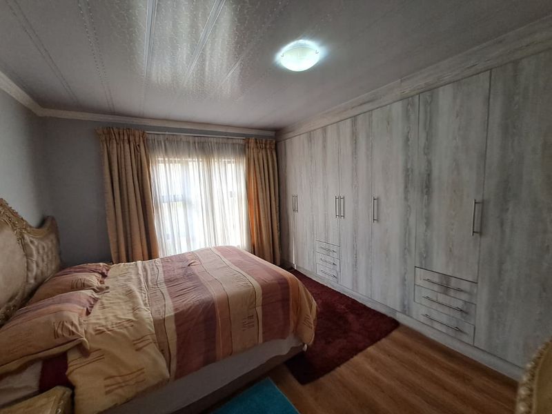 A well-maintained bedroom featuring extensive built-in cupboards with a light wood finish, laminate flooring, and a neutral color palette.