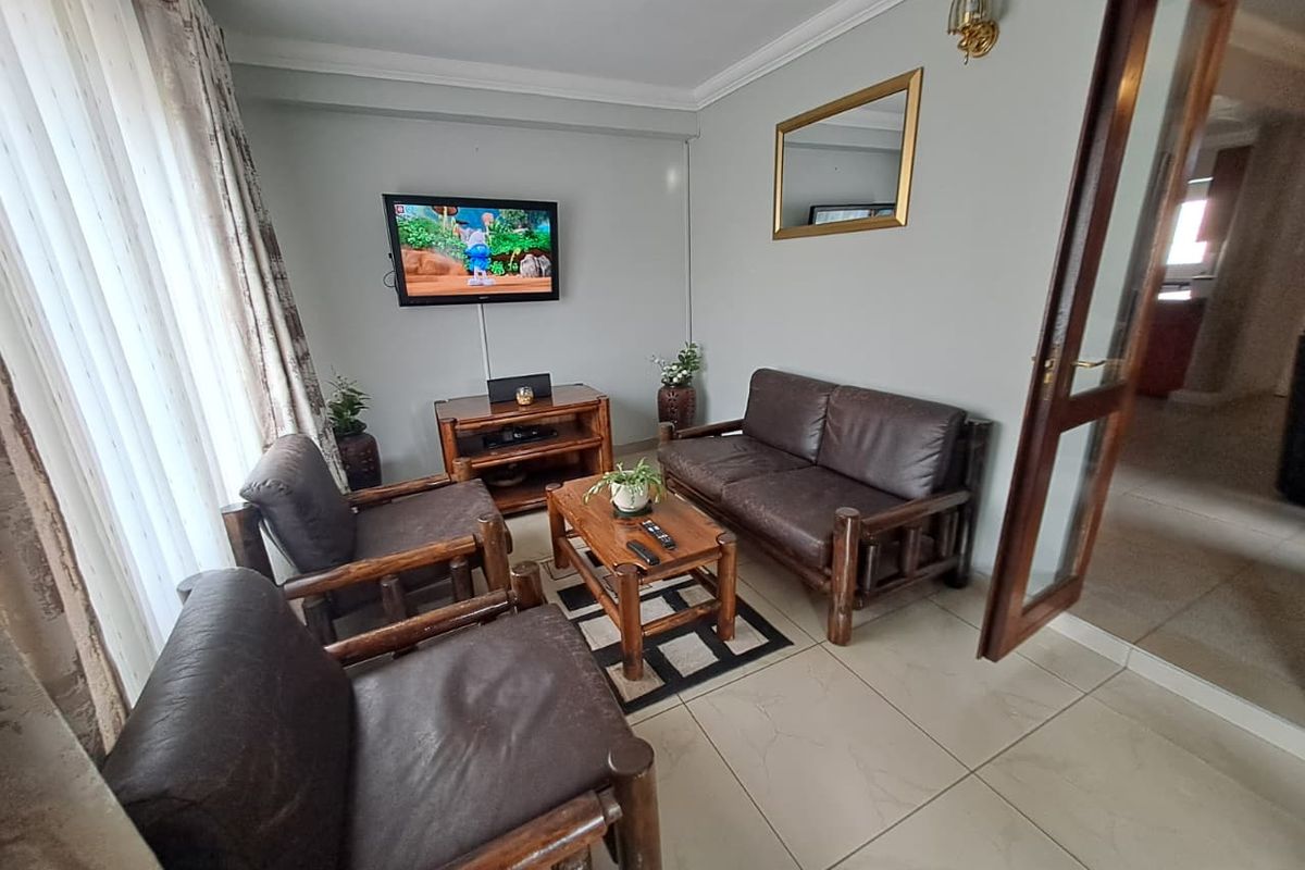 A comfortable living room featuring tiled flooring, crown molding, and a timber-framed glass door leading to adjacent spaces.