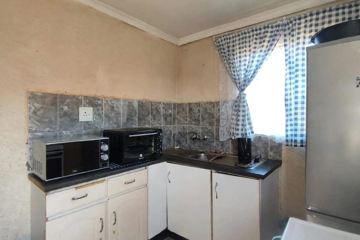 A compact kitchen featuring built-in cabinetry, a stainless steel sink, and tiled backsplash, currently requiring cosmetic updates to improve the overall aesthetic.