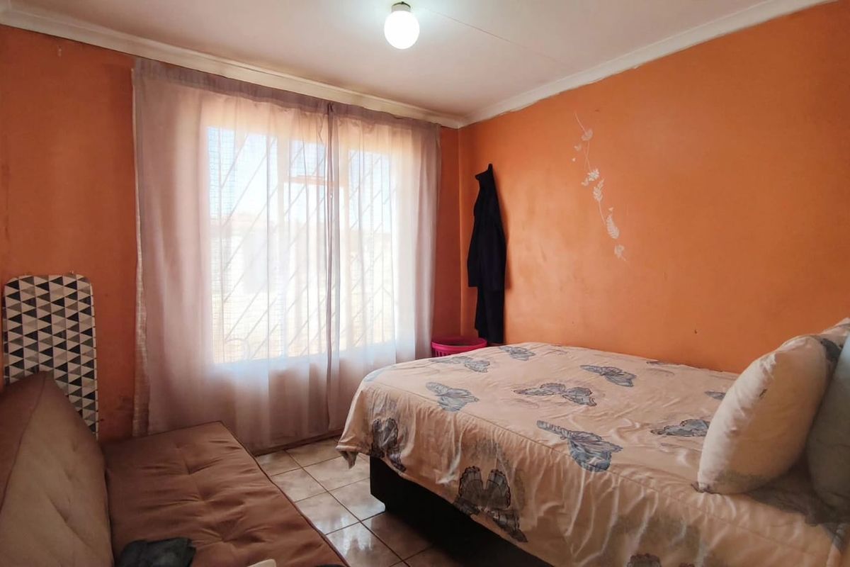 A compact bedroom featuring tiled flooring and a window fitted with security bars, currently finished with orange wall paint.