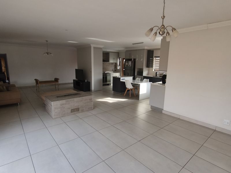 Spacious open-plan living and kitchen area featuring large format floor tiles, a central built-in fireplace, and modern kitchen cabinetry with an island.