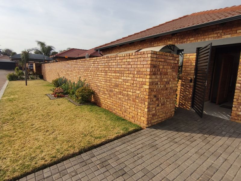 Front exterior view of the house featuring a face brick boundary wall, paved driveway, and a secure entrance gate.