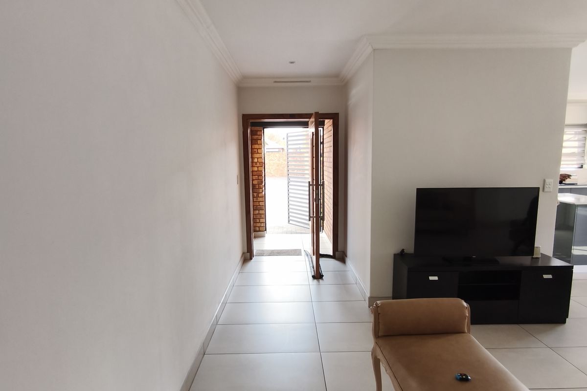 A bright living area featuring neutral tiled flooring and decorative cornicing, leading directly to the exterior entrance.