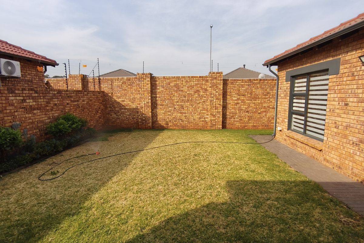 A well-maintained rear garden featuring a lawn, paved pathways, and secure face brick boundary walls with electric fencing.