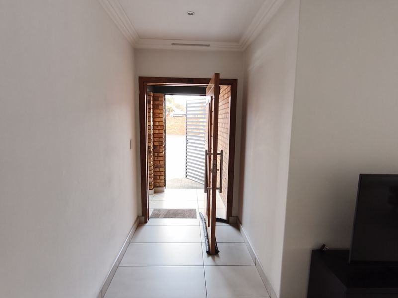 A bright and clean entrance hallway featuring neutral tiled flooring, crown molding, and a wooden door leading to the exterior.