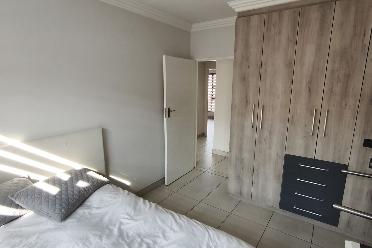 A well-maintained bedroom featuring neutral tiled flooring, modern built-in cupboards with integrated drawers, and classic ceiling cornice detailing.