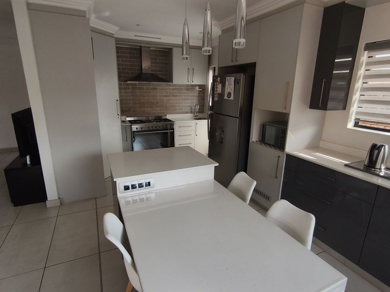 Modern kitchen featuring a central island, sleek cabinetry, built-in oven with extractor fan, tiled splashback, and neutral floor tiles.