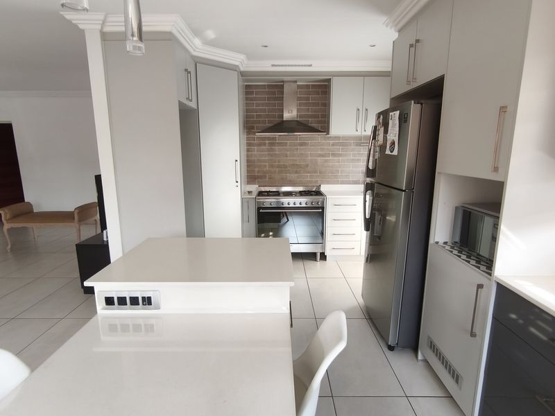 Modern kitchen featuring stone countertops, built-in cabinetry, gas stove with extractor fan, and tiled flooring, seamlessly flowing into the adjacent living area.