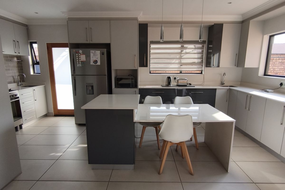 Modern kitchen featuring sleek two-tone cabinetry, stone countertops, integrated appliances, tiled flooring, and a central island with an attached dining area.
