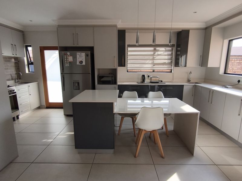 Modern kitchen featuring sleek two-tone cabinetry, stone countertops, integrated appliances, tiled flooring, and a central island with an attached dining area.