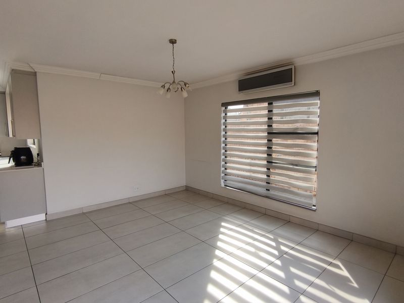 A bright, open-plan living area featuring neutral tiled flooring, a split-system air conditioner, and modern window blinds, offering a clean and versatile space.
