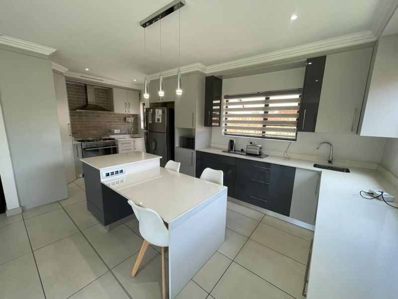 Modern kitchen featuring sleek two-tone cabinetry, stone countertops, a central island, and high-quality built-in appliances with contemporary finishes.