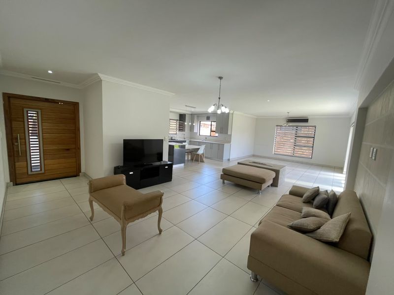 Spacious open-plan living area featuring large format floor tiles, modern kitchen cabinetry, recessed lighting, and a solid timber entrance door.