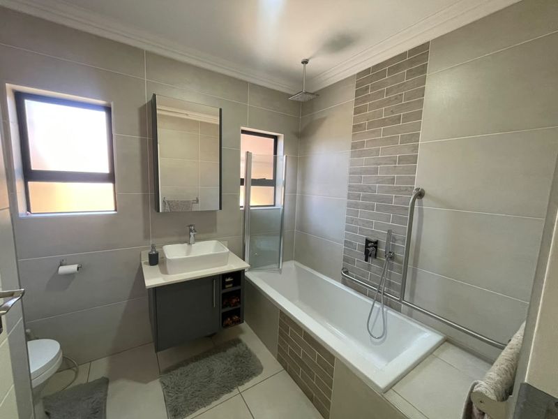 Modern bathroom featuring a vessel sink vanity, bathtub with shower combination, contemporary wall tiling, and safety grab bars.