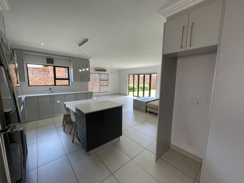 Spacious open-plan living and kitchen area featuring modern cabinetry, a central island, tiled flooring, and large sliding doors leading to the garden.