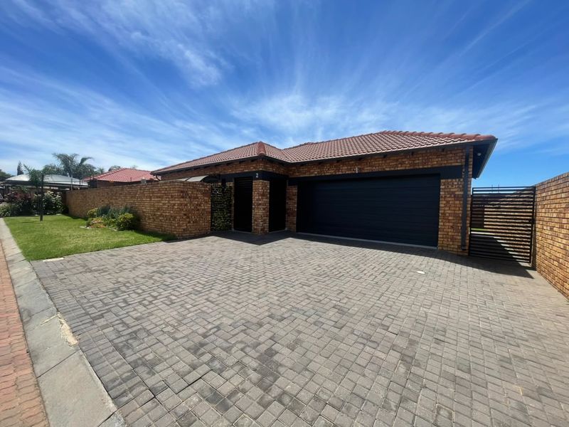 Front view of a well-maintained face brick house featuring a double garage, paved driveway, and secure boundary walling.