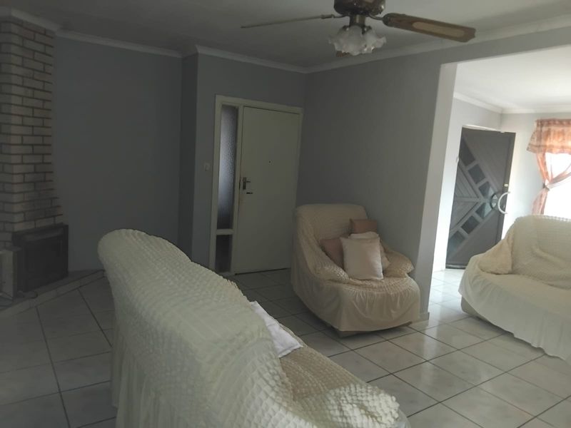 Living room featuring tiled flooring, a brick fireplace, and a ceiling fan, with an open layout leading to an adjacent entrance area.