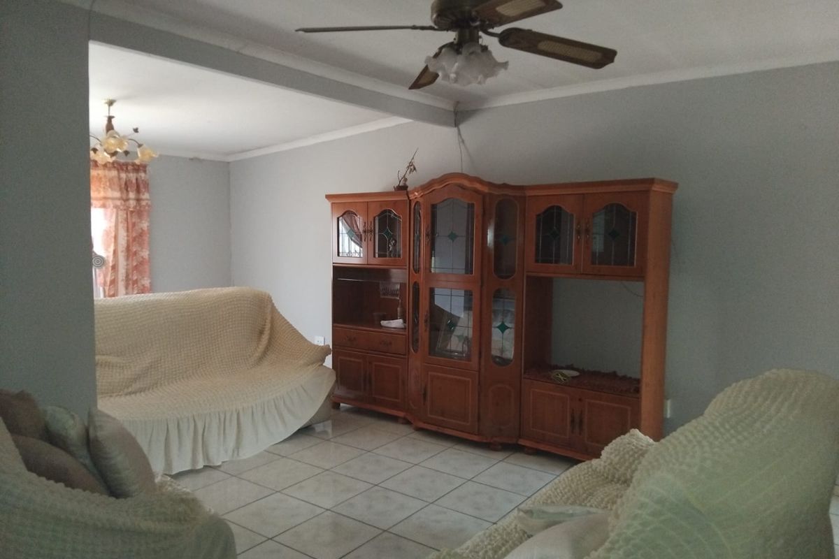 A living room area featuring tiled flooring and a ceiling fan, with an open-plan layout connecting to an adjacent space.
