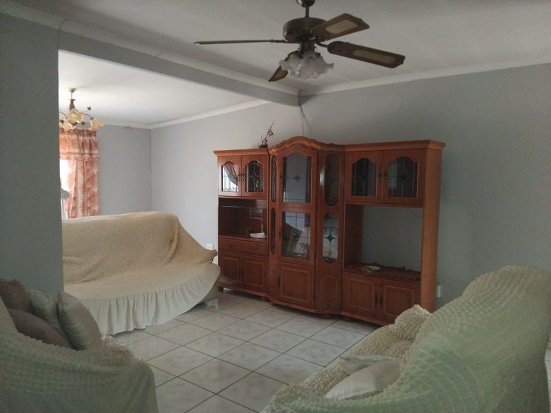 A living room area featuring tiled flooring and a ceiling fan, with an open-plan layout connecting to an adjacent space.
