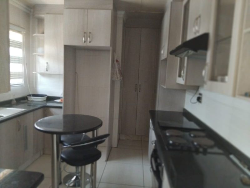 A functional kitchen featuring built-in cabinetry, dark countertops, a hob, an extractor fan, and tiled flooring.