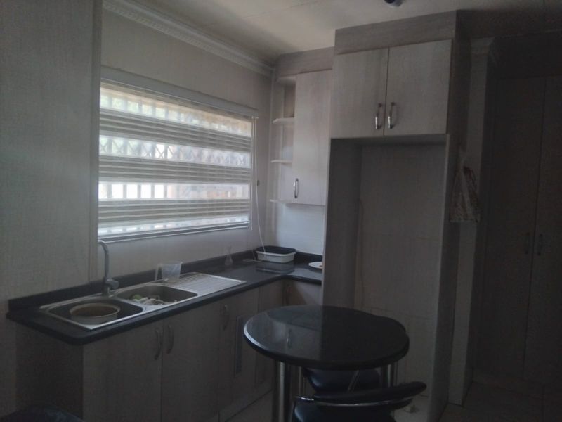 A functional kitchen featuring built-in cabinetry, dark countertops, and a double sink, with natural light entering through a window with fitted blinds.
