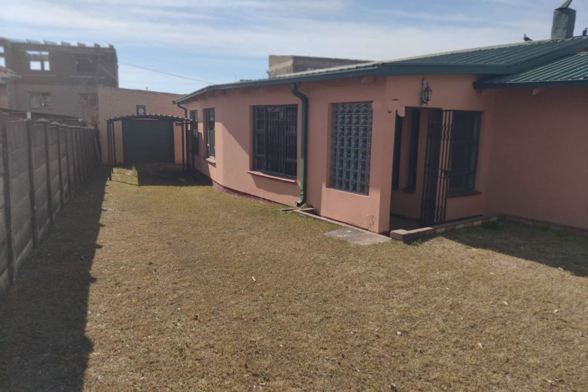Rear view of the property featuring a metal roof, security bars on windows, a glass block feature, and a detached carport within a fenced yard.
