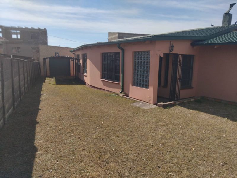 Rear view of the property featuring a metal roof, security bars on windows, a glass block feature, and a detached carport within a fenced yard.