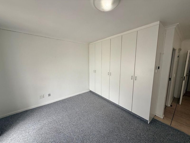 A clean, empty bedroom featuring neutral walls, grey carpet flooring, and extensive white built-in cupboards providing ample storage space.