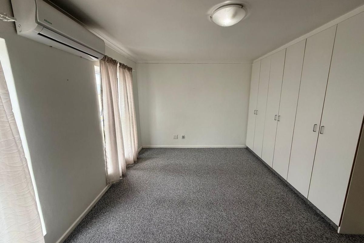 A spacious, empty bedroom featuring neutral carpeting, extensive built-in storage cupboards, and a wall-mounted air conditioning unit.