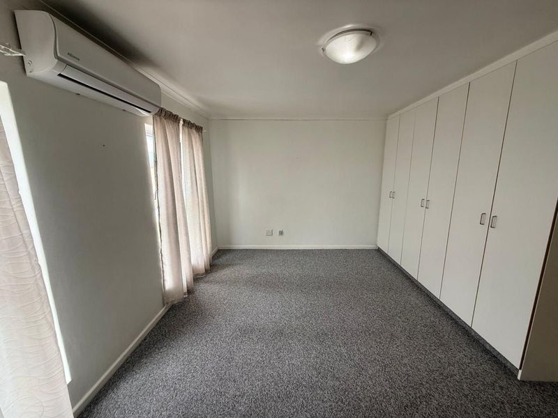 A spacious, empty bedroom featuring neutral carpeting, extensive built-in storage cupboards, and a wall-mounted air conditioning unit.