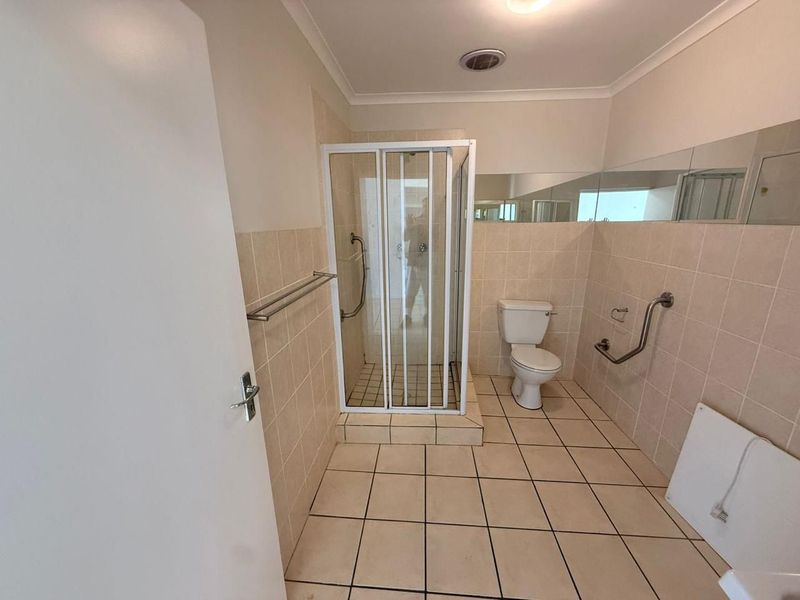 A functional bathroom featuring a shower enclosure, toilet, and safety grab rails, finished with neutral wall and floor tiling.