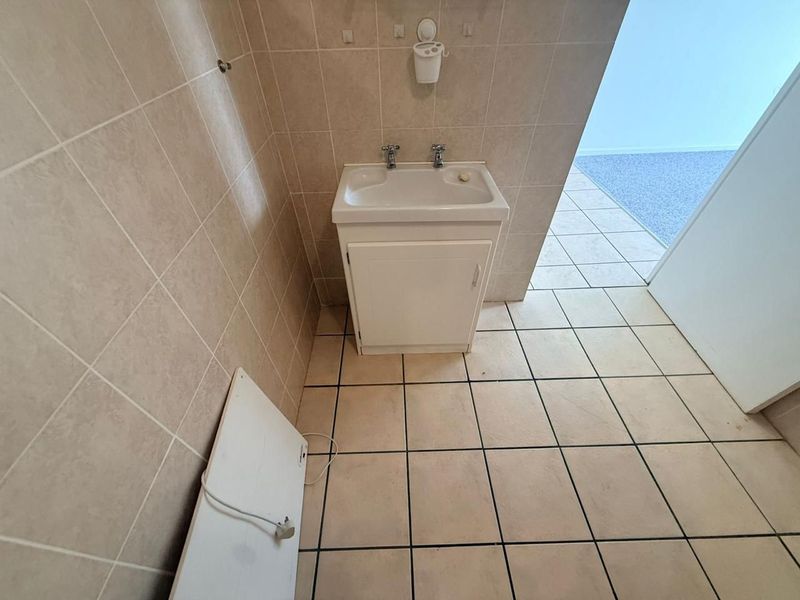 A functional bathroom featuring a vanity cabinet with a basin, tiled flooring, and wall tiling throughout.