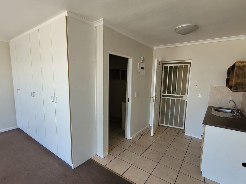 Open plan living area featuring built-in cupboards, a kitchenette with sink, tiled flooring, and a security gate leading to the entrance.