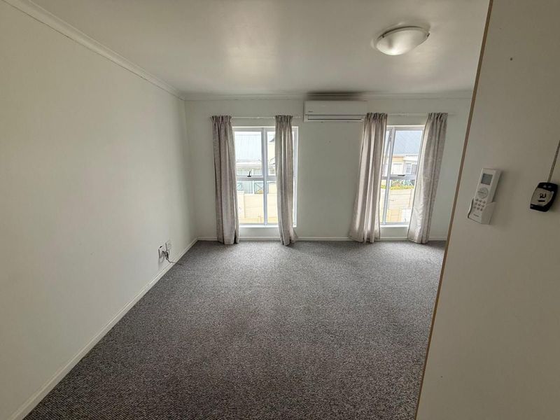 A bright, empty bedroom featuring neutral carpet flooring, dual windows, and a wall-mounted split-system air conditioning unit.