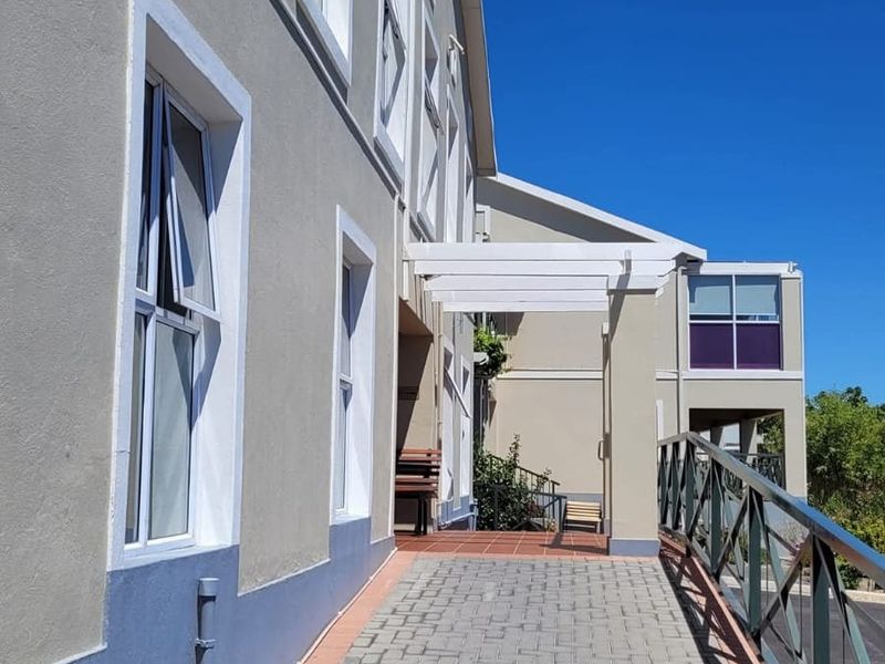 Exterior view of the apartment building featuring a paved walkway, metal safety railing, and a pergola structure over the entrance path.