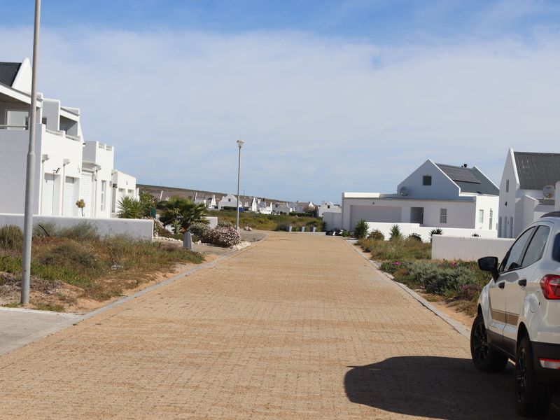 A view of the residential street and driveway approach within a coastal estate, featuring white architectural facades and paved access roads.