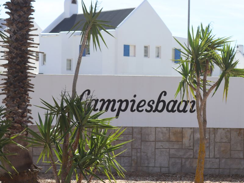 A view of the estate entrance featuring a stone-clad boundary wall with signage and landscaped palm trees.