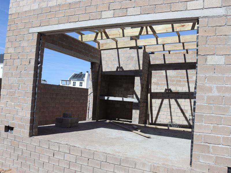 An unfinished outdoor patio area under construction, featuring exposed concrete block walls, timber roof trusses, and a built-in masonry braai structure.
