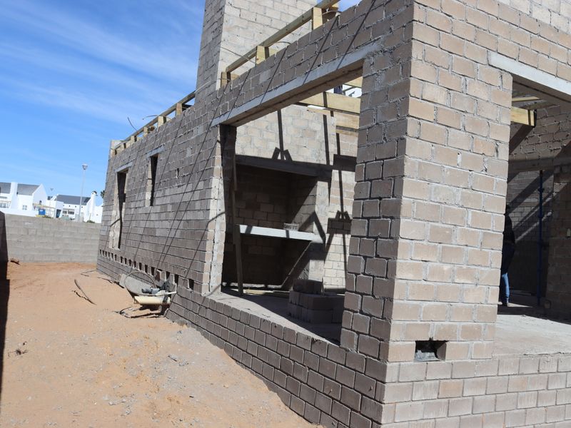 A rear view of a residential property currently under construction, featuring exposed concrete block walls and timber roof framing.