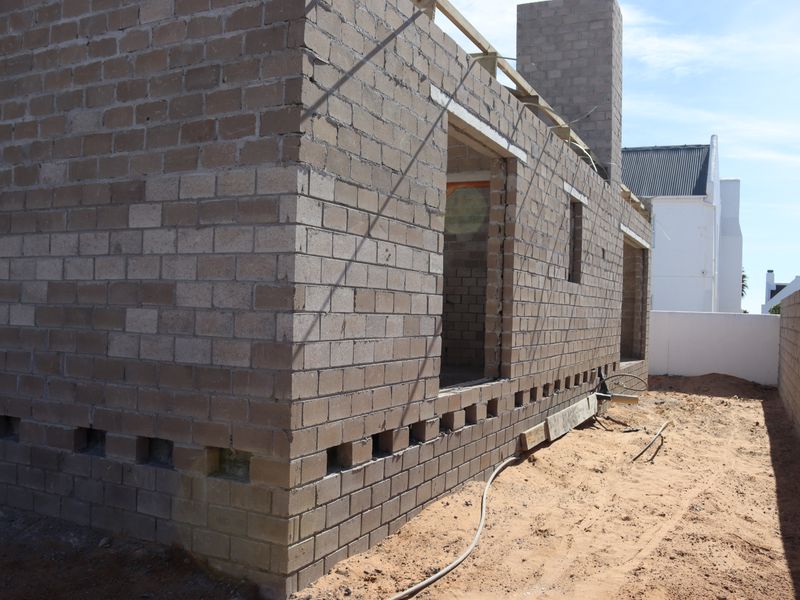 A view of a property under construction, featuring exposed concrete block walls, a chimney stack, and open window and door frames.