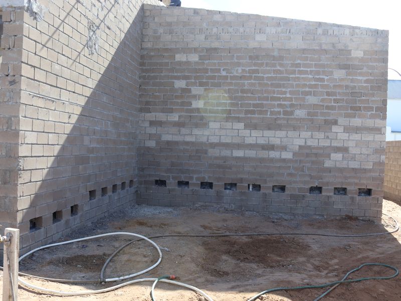 An unfinished rear exterior area showing exposed brickwork walls with weep holes and an external water tap, currently under construction.